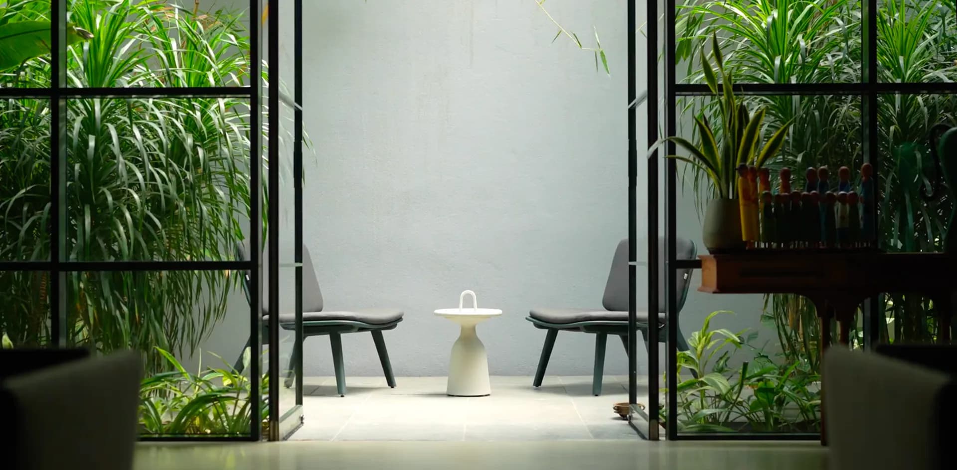Lush indoor plants framing a sunlit seating nook behind glass doors