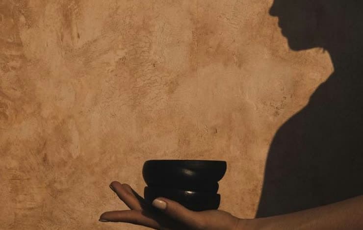 Hands holding a smooth dark stone against a warm textured backdrop